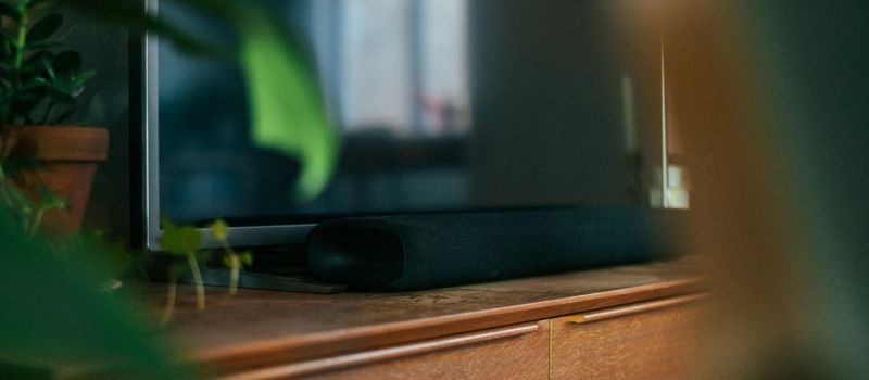 Hvad skal du være opmærksom på, når du køber en soundbar? nærbillede af et fjernsyn omgivet af planter oven på et tv-møbel med en soundbar under fjernsynet