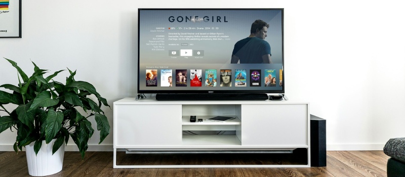 Få det bedste ud af din soundbar med standarder fra Vebos en sort tv inklusive soundbar oven på et hvidt tv-møbel med en grøn plante til venstre for tv'et